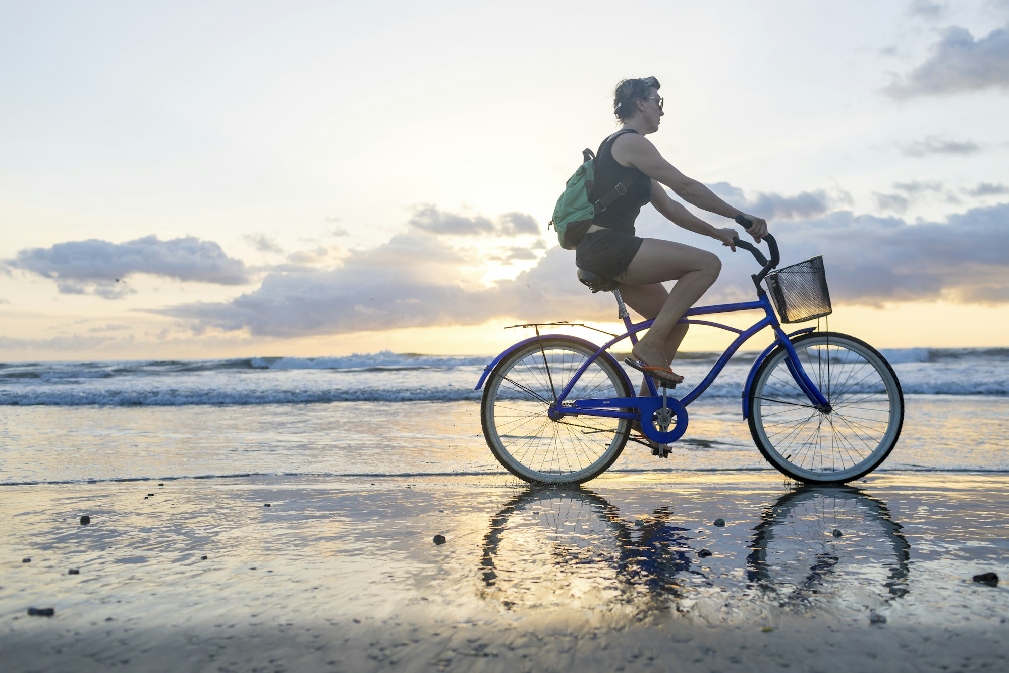 Woman cycling on beach at sunset, Nosara, Guanacaste Province, Costa Rica